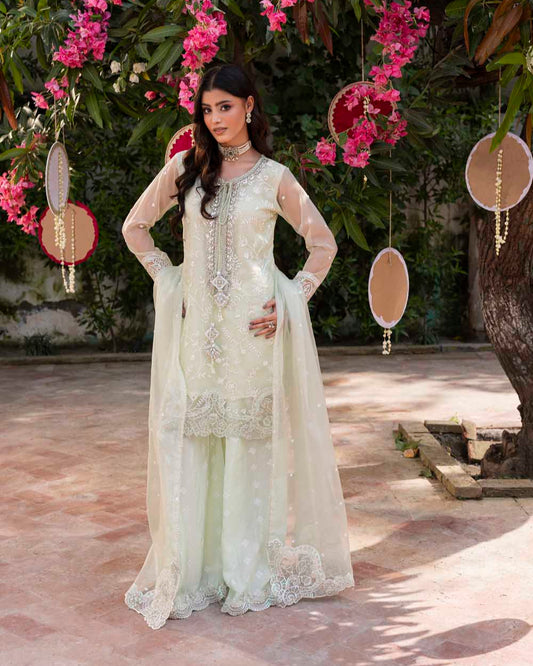 Woman in a white embroidered outfit standing in front of pink flowers and greenery.