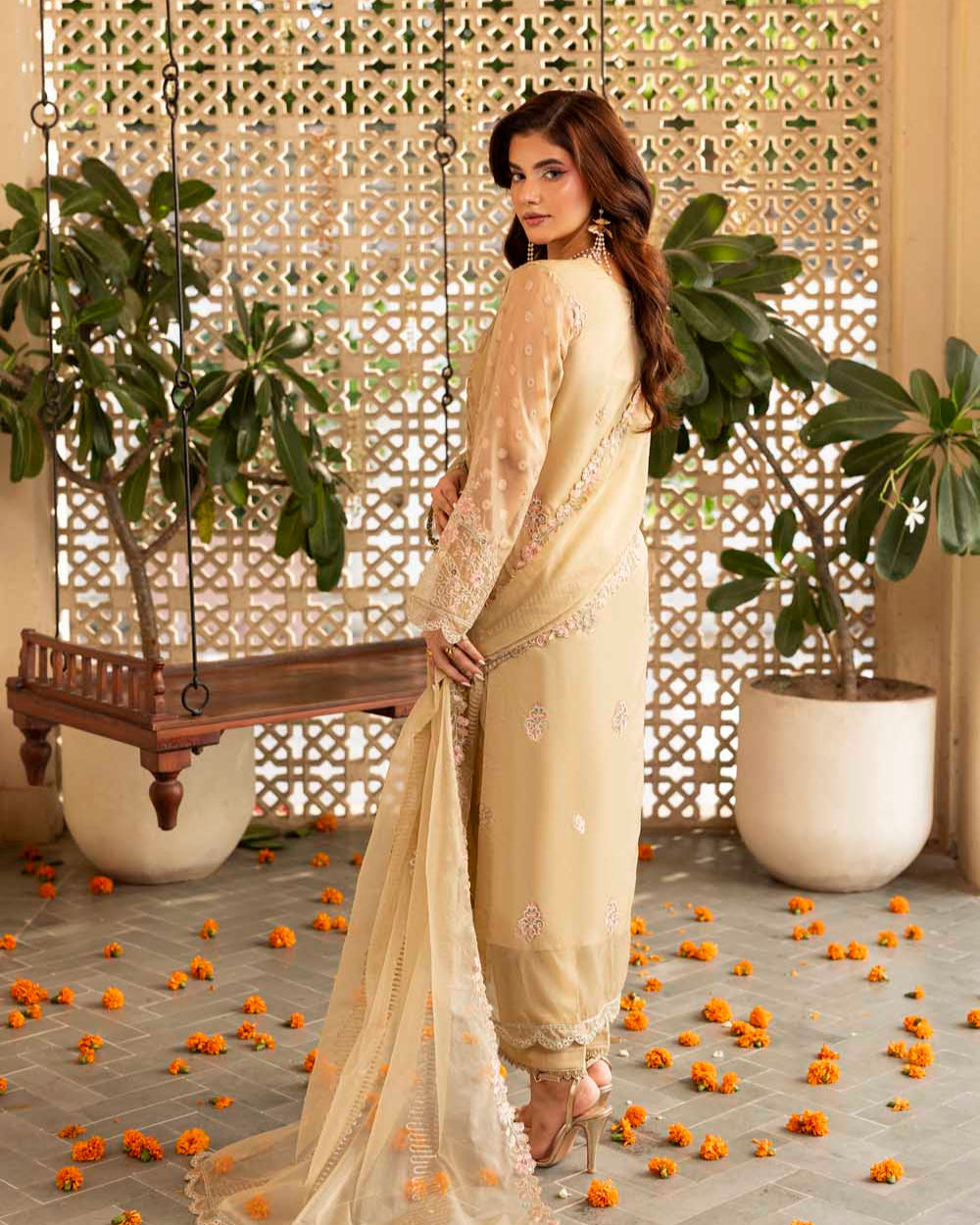 Woman in a cream saree standing in a decorated room with plants and decorative elements.