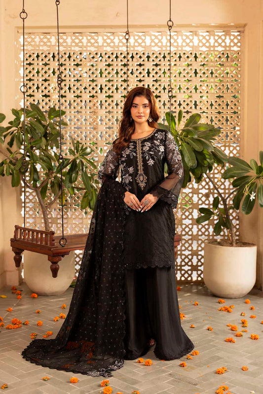 Woman in a black traditional outfit with floral patterns standing in a decorated indoor setting.
