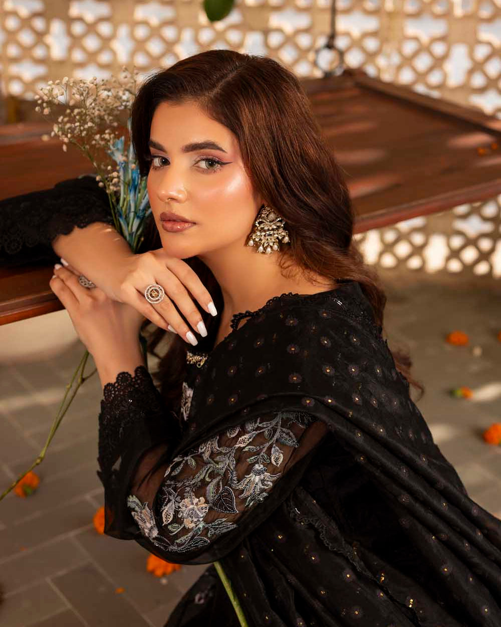 Woman in a black embroidered dress sitting outdoors with decorative elements.