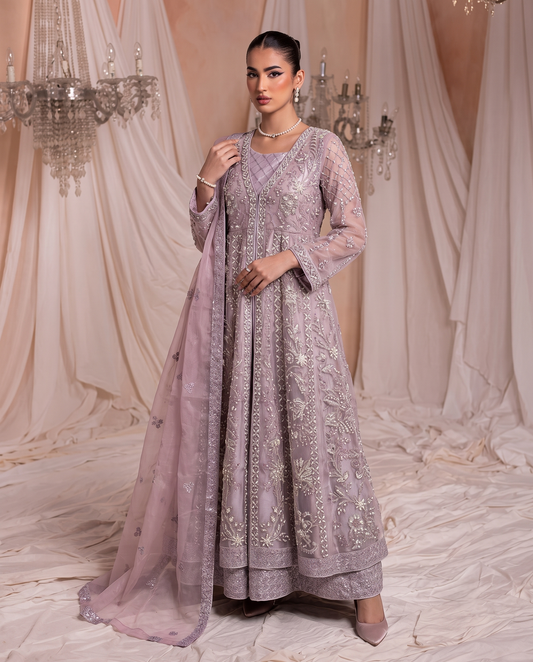 A woman models a lavender purple embroidered Anarkali suit with a matching dupatta in a draped studio setting with chandeliers.