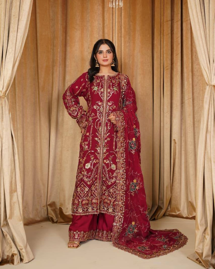 Woman in a red embroidered traditional outfit standing in front of beige curtains.