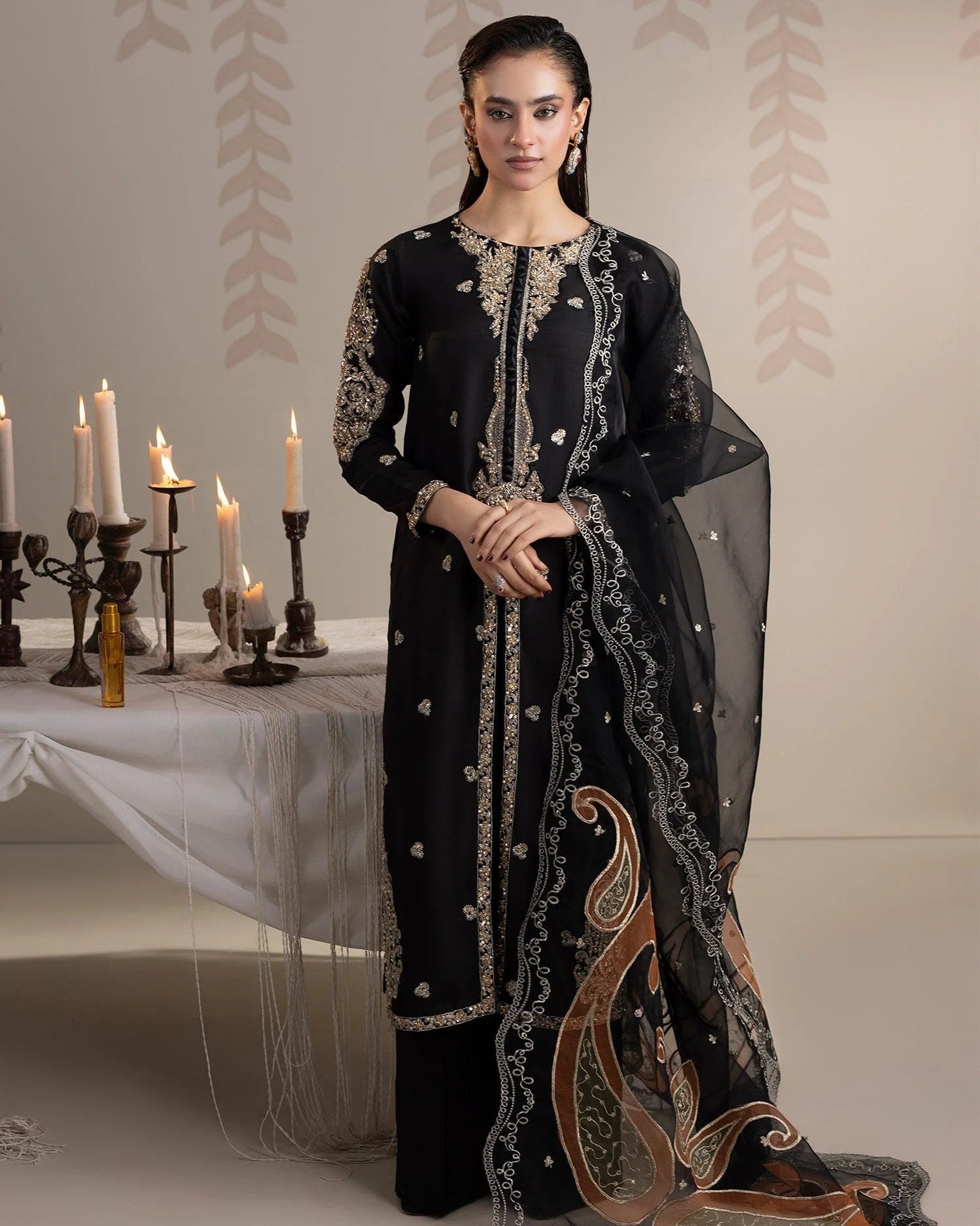 Woman in a black embroidered outfit standing in front of a decorated table with candles.