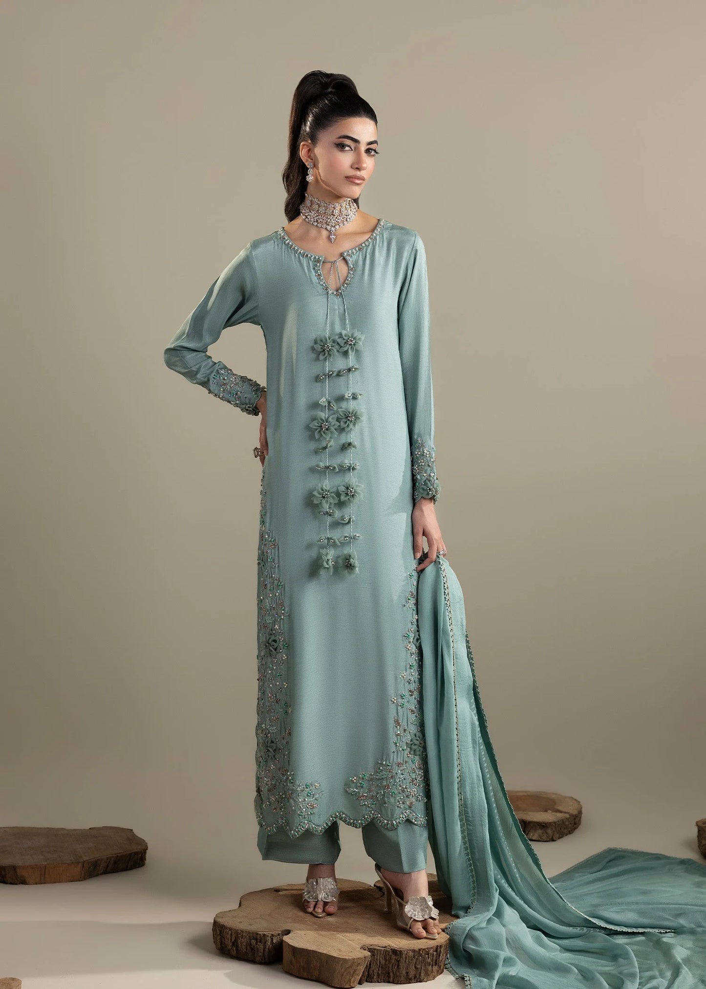 Woman wearing a light blue embroidered traditional outfit with a plain background