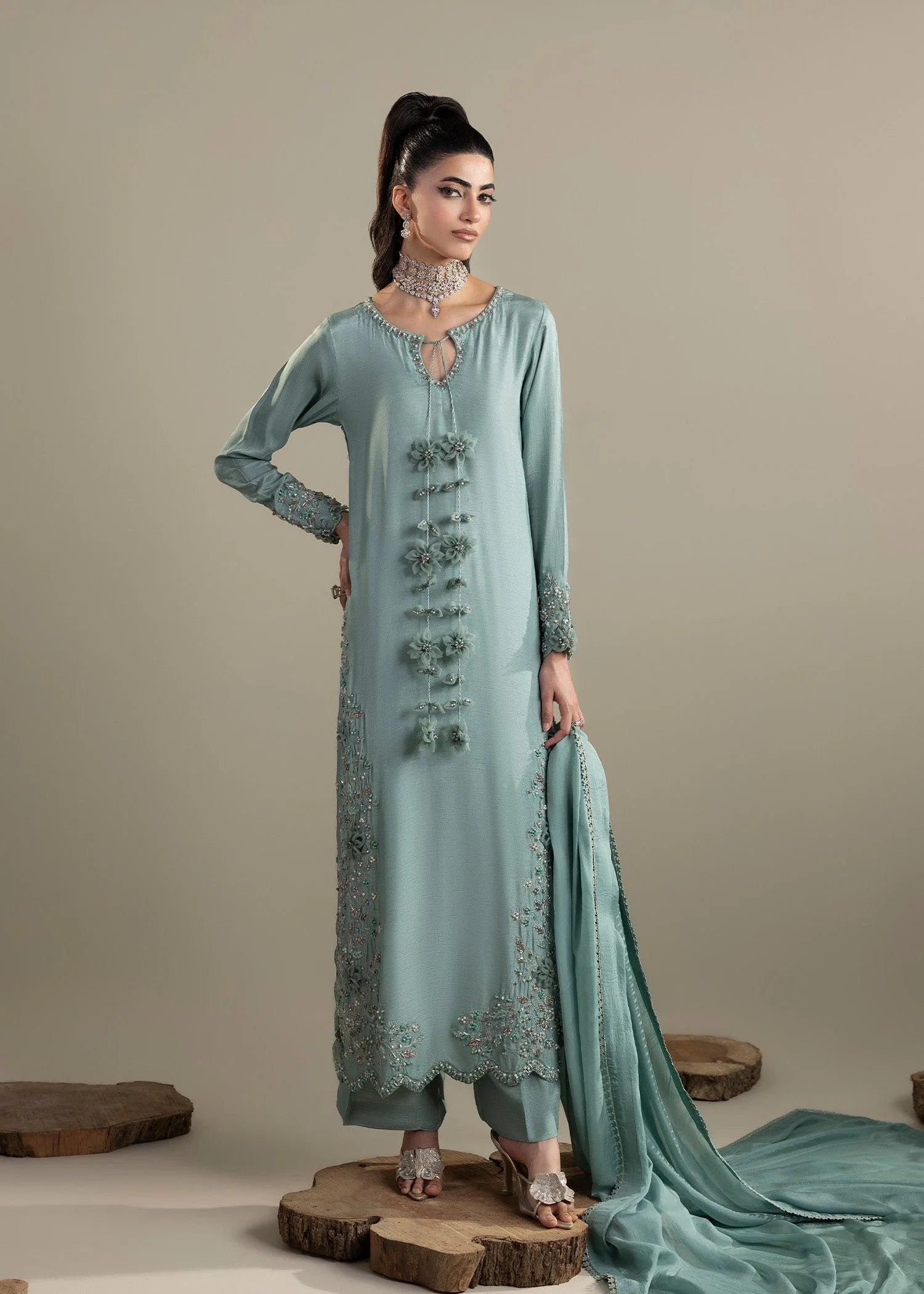 Woman wearing a light blue embroidered traditional outfit with a plain background