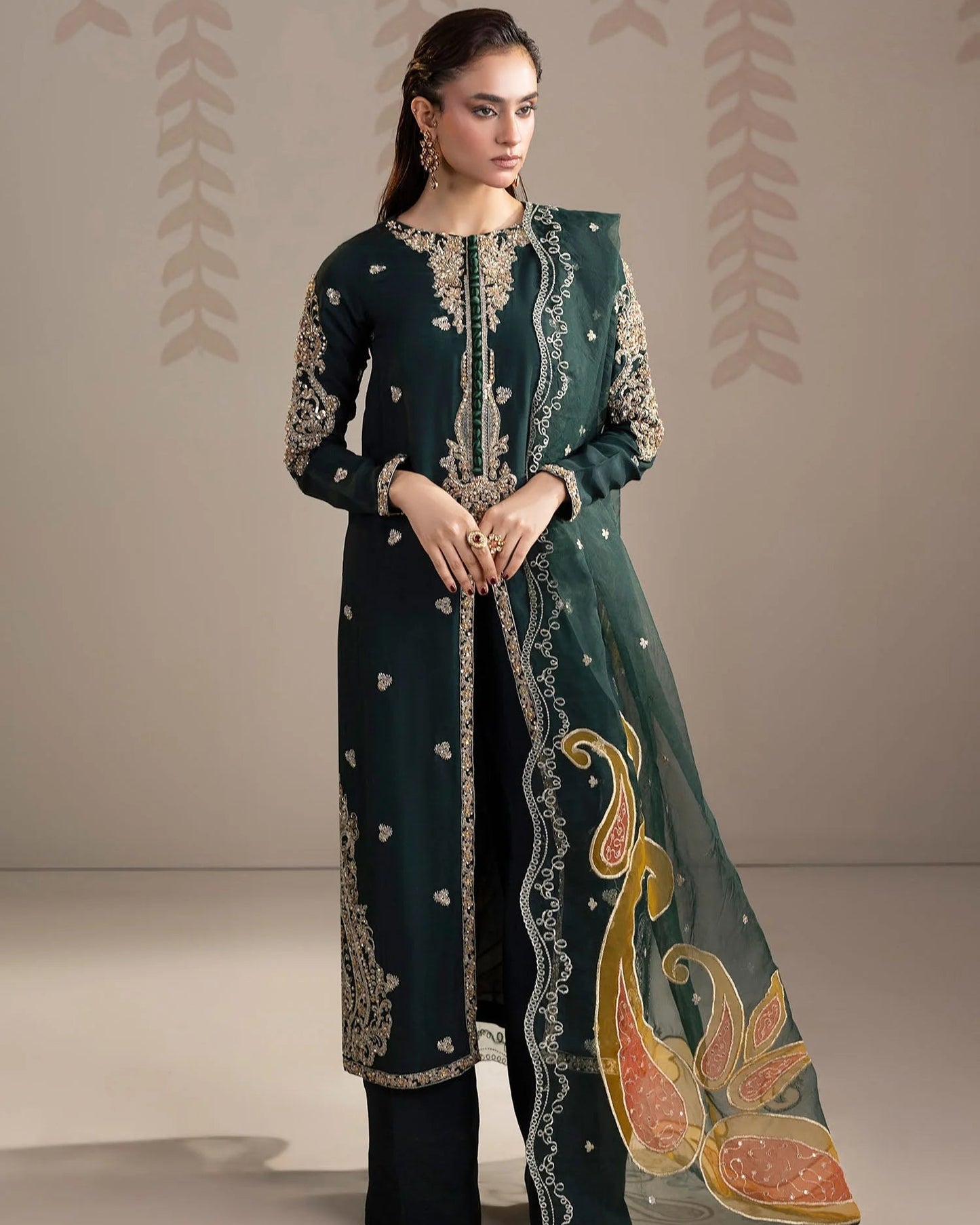 Woman wearing a dark green embroidered outfit with a matching dupatta on a beige background